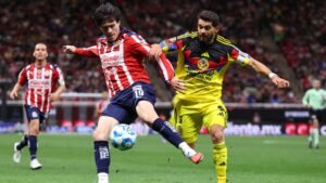 Chivas player in red and white stripes competes for the ball against Club América’s yellow-clad goalkeeper in a tense match moment.