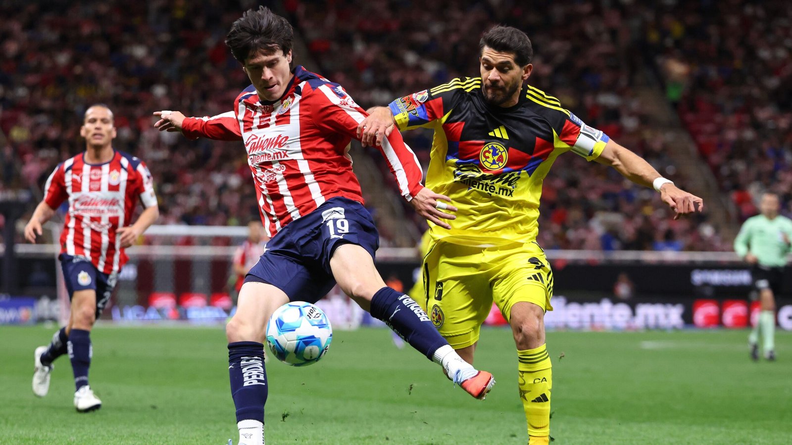 Chivas player in red and white stripes competes for the ball against Club América’s yellow-clad goalkeeper in a tense match moment.