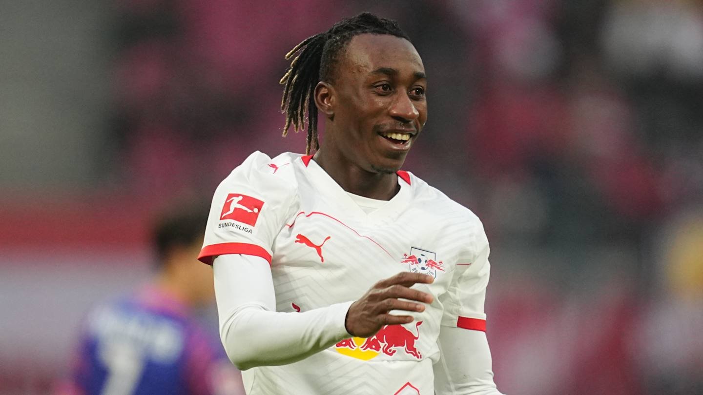 Excited player from RB Leipzig celebrating a goal, wearing a white kit with red accents, against a blurred stadium background.