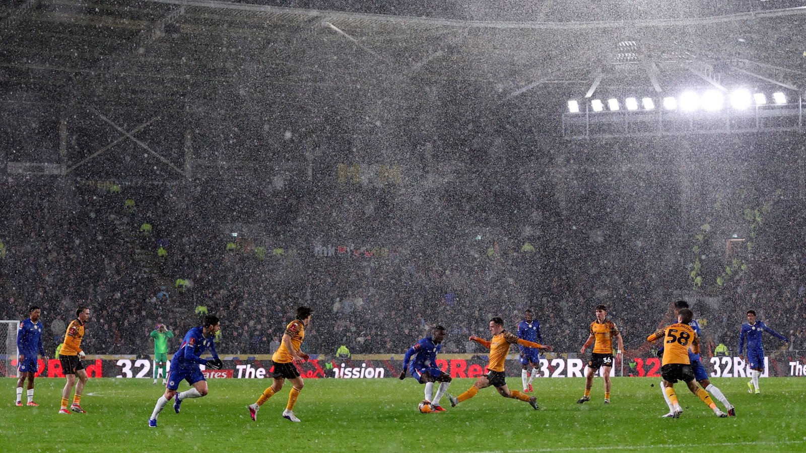 Tijdens een gespannen moment in de wedstrijd valt er hevige regen, waarbij Hull City-spelers in amber en zwart tegen hun tegenstanders in het blauw spelen.