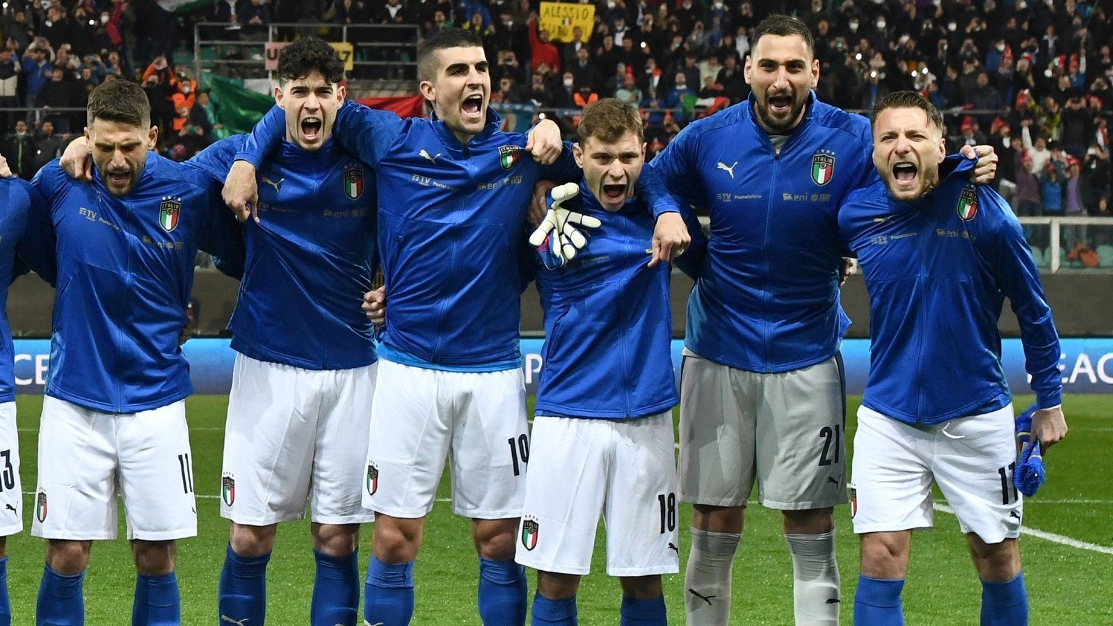 Spelers van het Italiaanse nationale voetbalteam die tijdens het volkslied juichen, in blauwe tenues, en opwinding en kameraadschap tonen.
