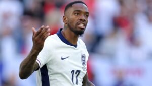 Ivan Toney gestures during an England match, wearing the team's white kit with the Three Lions emblem, showcasing determination on the pitch.