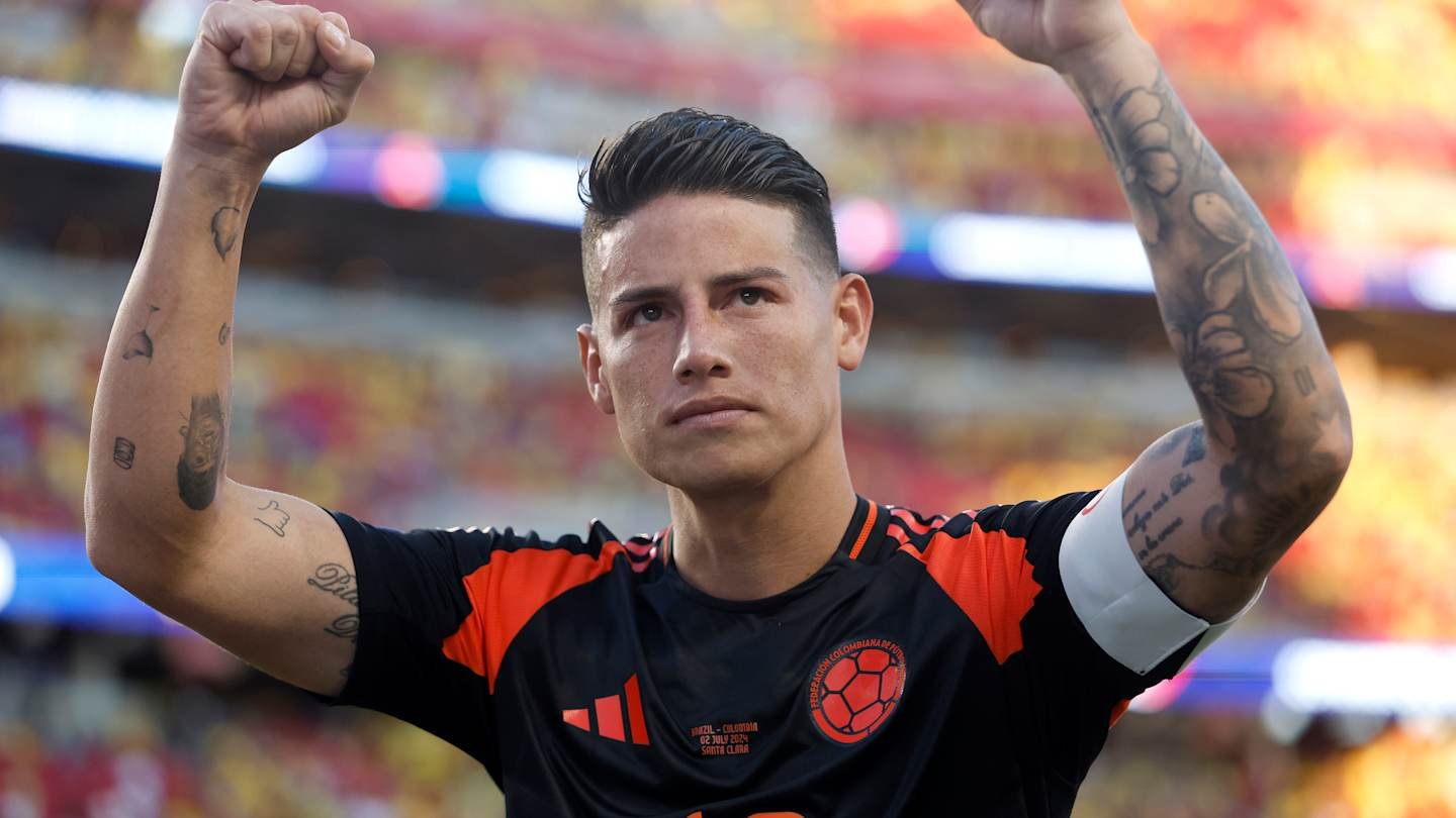 James Rodriguez, in Colombia's black and orange kit, celebrates with clenched fists, showcasing his tattoos in a vibrant stadium atmosphere.