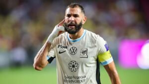 Karim Benzema, wearing Ittihad Jeddah's light blue kit and captain's armband, gestures towards fans after a match celebration.