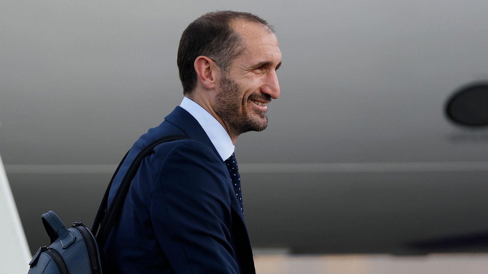 Giorgio Chiellini in a navy suit, smiling, as he arrives at a venue, showcasing professionalism and team spirit.