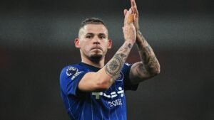 Kalvin Phillips, vêtu d'un maillot bleu du club, salue les supporters avec une expression sérieuse, laissant voir ses tatouages lors d'un match.