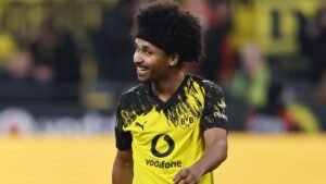 Karim Adeyemi smiles while wearing Borussia Dortmund's vibrant yellow and black kit during a match, showcasing team spirit.