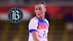Keira Barry, vêtue du maillot de l'Angleterre avec des accents bleus et rouges, est en appui sur le terrain aux côtés du logo du Bay Football Club.