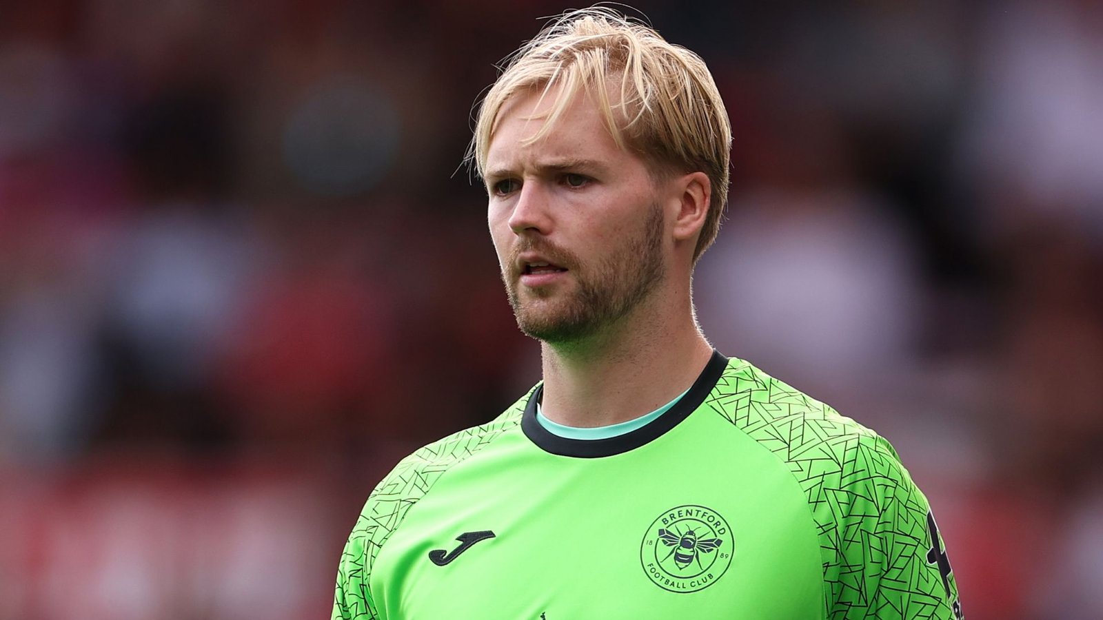 Le gardien de Brentford, Kelleher, vêtu d'un maillot vert vif, concentré sur le match, fait preuve de détermination sur le terrain.