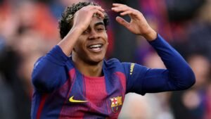 Lamine Yamal esquisse un geste en souriant pendant un match, portant le maillot rayé bleu et grenat emblématique du Barça, manifestant son enthousiasme.