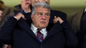 Joan Laporta ajustant sa veste dans les tribunes, l'expression concentrée au milieu de la foule, illustrant son rôle dans la direction du FC Barcelone.