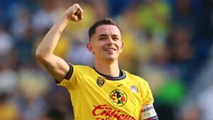 Celebrating player in a yellow América jersey, fist raised in triumph, showcasing excitement during a Liga MX match.