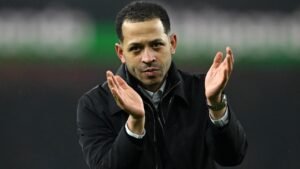 Liam Rosenior applaudit en bord de terrain, habillé d'un manteau noir, démontrant sa passion pour le jeu pendant un match.