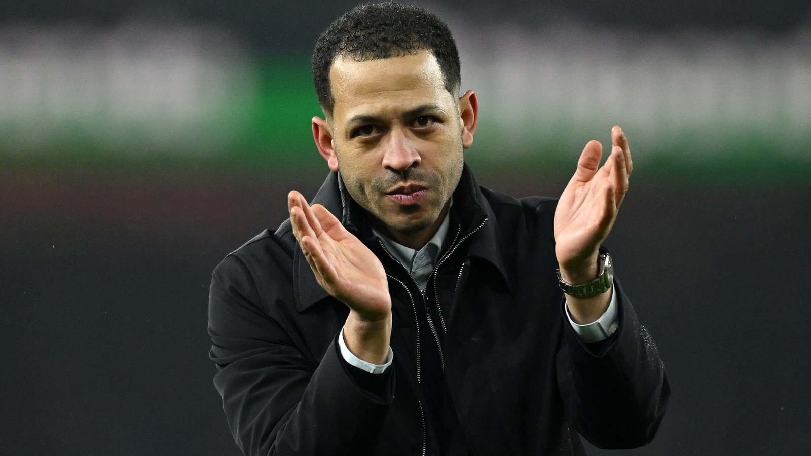 Liam Rosenior applaudit en bord de terrain, habillé d'un manteau noir, démontrant sa passion pour le jeu pendant un match.