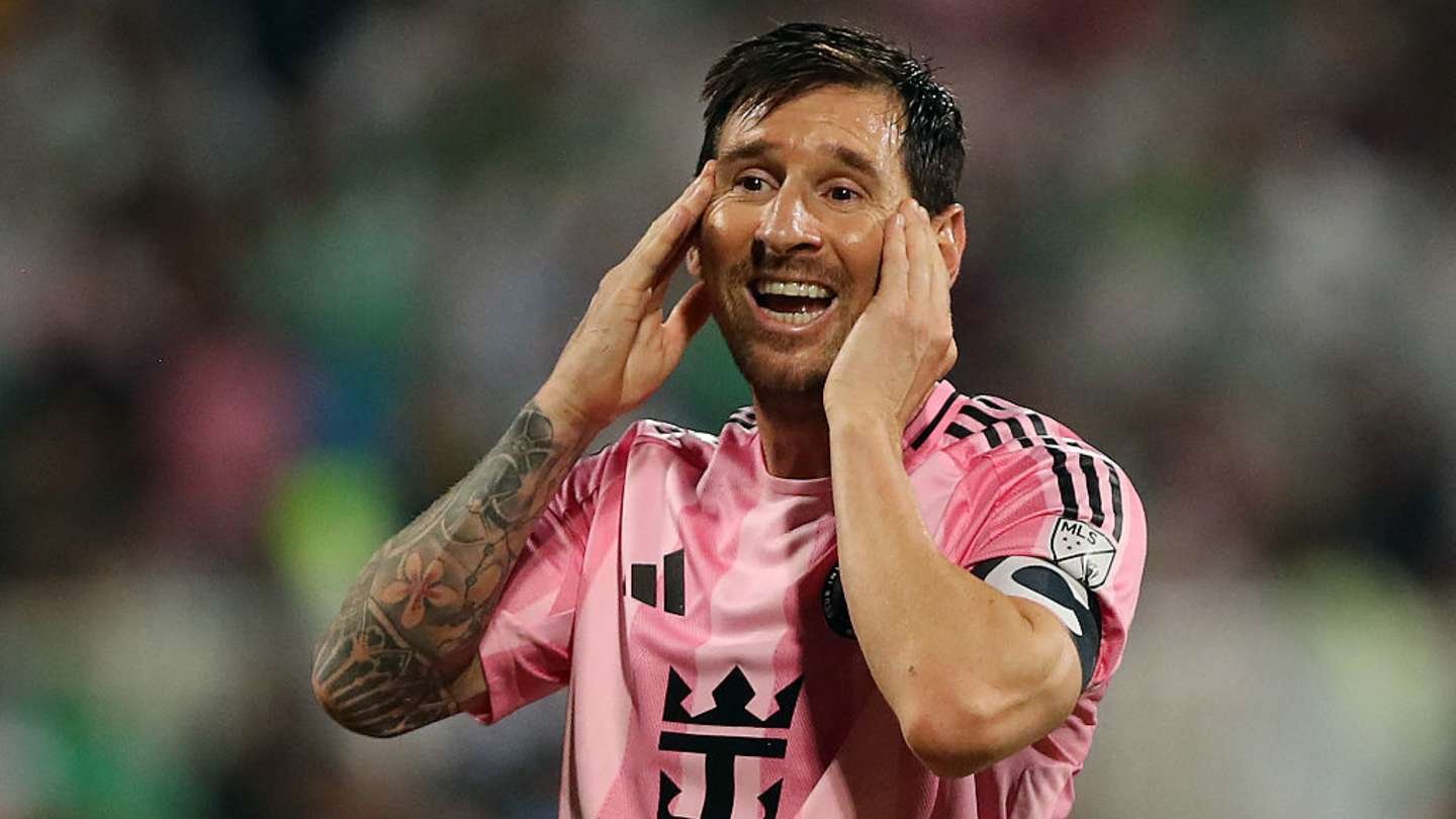 Lionel Messi in a pink football kit, expressing frustration during a match. Background features blurred stadium atmosphere.