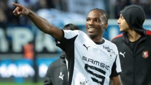 Rennes player smiling and pointing, wearing a black and white jersey, celebrating a moment after a match.