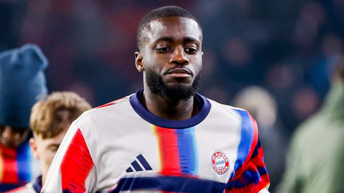 Un joueur du Bayern Munich, l'air sérieux, portant un haut d'entraînement multicolore, sur le terrain avant un match.