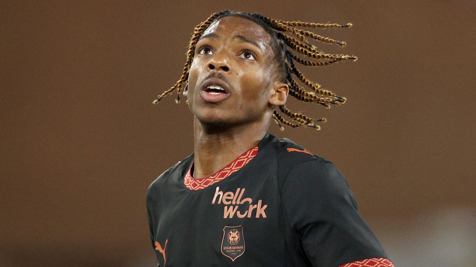 Jeremy Jacquet, gekleed in een zwart voetbaltenue met oranje accenten, kijkt geconcentreerd omhoog tijdens een wedstrijd voor zijn team.