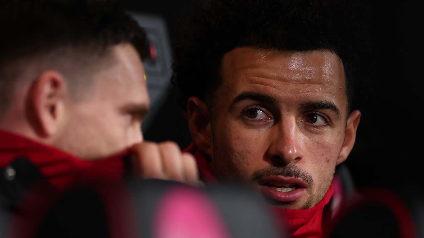 Liverpool players in discussion during a match, with one player focused and looking towards the camera, showcasing team camaraderie.