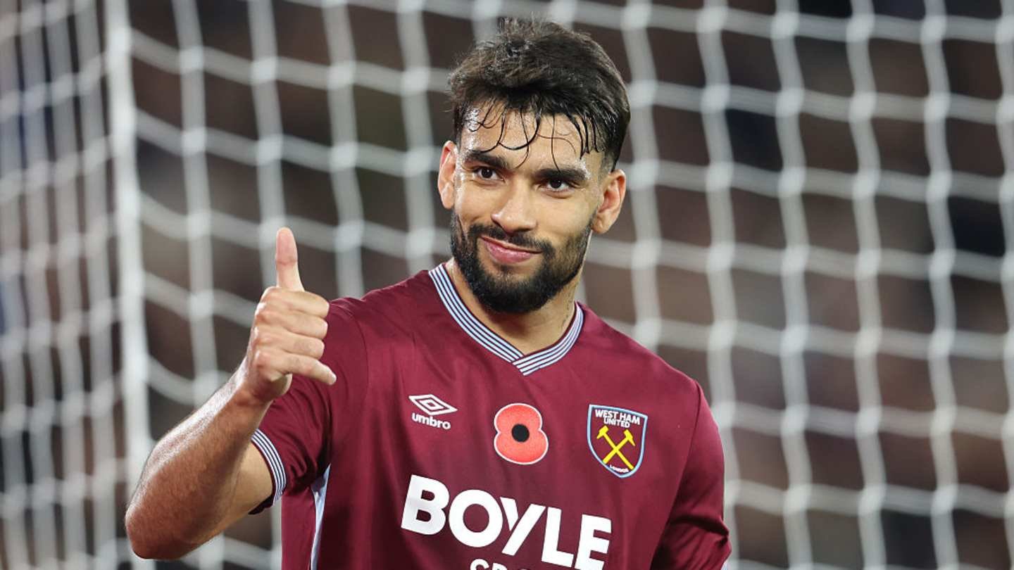 Lucas Paquetá celebrates in a maroon West Ham United kit, giving a thumbs up, with a football goal net in the background.