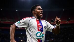 Lyon player celebrates passionately in white and red kit after scoring, highlighting excitement in a match context.