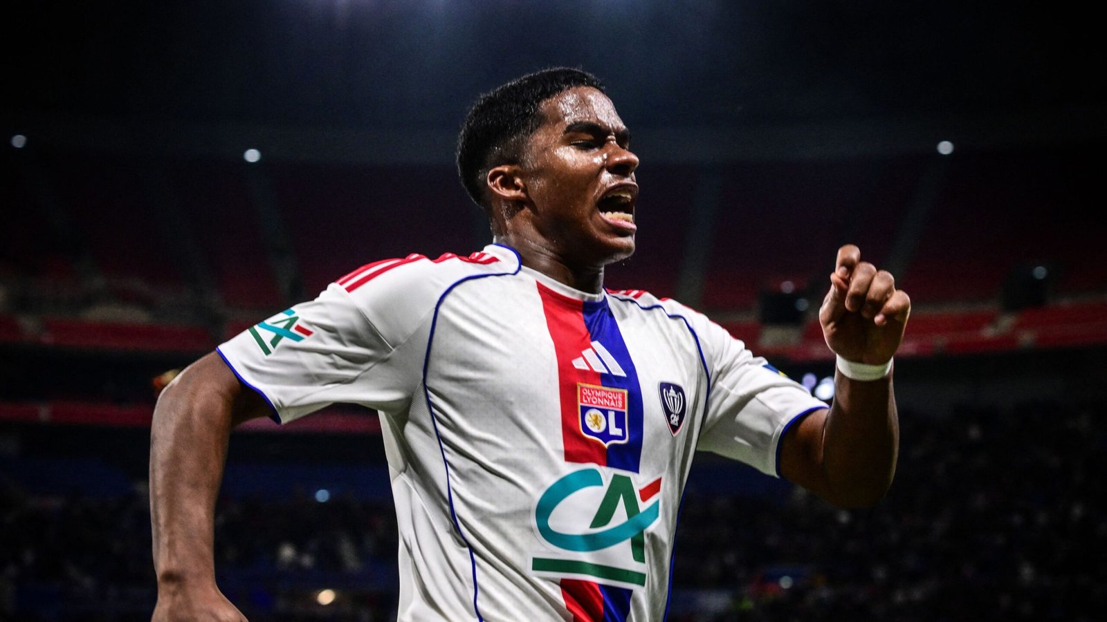 Lyon player celebrates passionately in white and red kit after scoring, highlighting excitement in a match context.