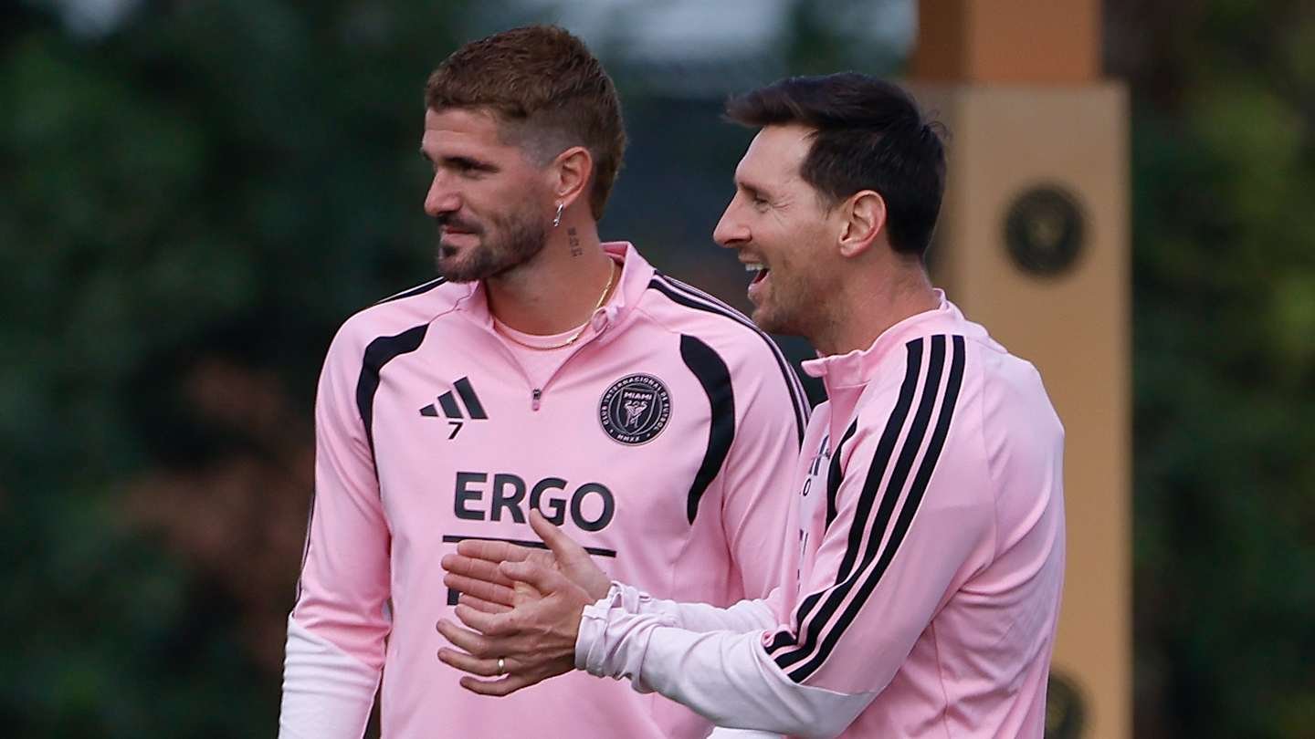 Lionel Messi and a teammate in pink Inter Miami training kits, sharing a light moment during a practice session.