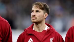 Liverpool's midfielder Mac Allister, dressed in a red training jacket, gazes thoughtfully during a match warm-up.
