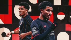 Malik Tillman in het tenue van Bayer Leverkusen gebaart met een opgeheven vinger, tegen een achtergrond met gedurfde, contrasterende kleuren.