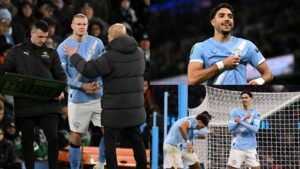 Manchester City players celebrate a goal in the Carabao Cup match against Newcastle, with coach Pep Guardiola and Erling Haaland on the sidelines.