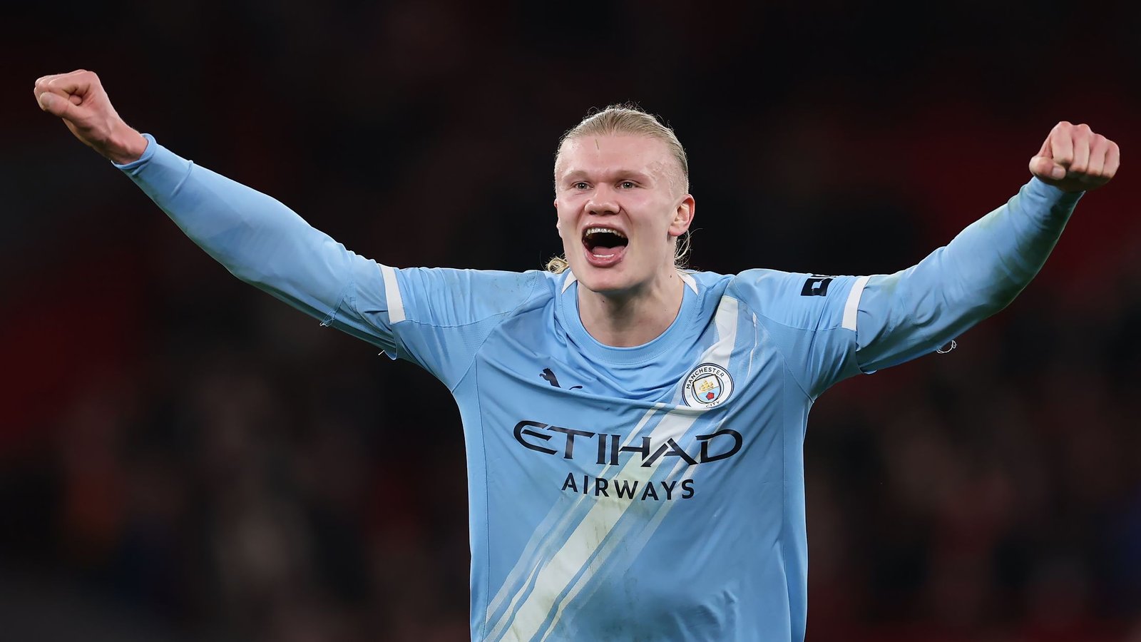 Erling Haaland célébrant avec passion dans le maillot bleu clair de Manchester City après un but, exhibant ses cheveux longs distinctifs et son exaltation.