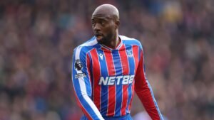 Malik Mateta dans le maillot rouge et bleu de Crystal Palace, concentré pendant un match, démontrant sa détermination sur le terrain.