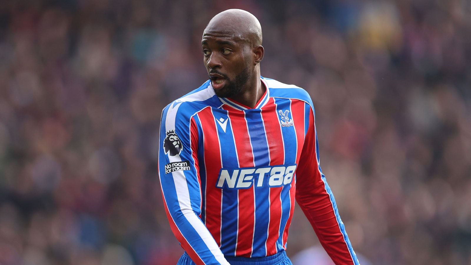 Malik Mateta dans le maillot rouge et bleu de Crystal Palace, concentré pendant un match, démontrant sa détermination sur le terrain.