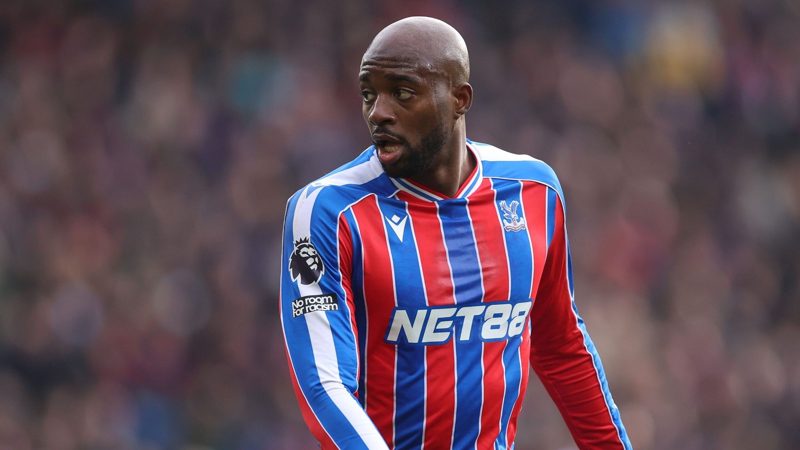 Crystal Palace player Jean-Philippe Mateta in red and blue kit, looking focused on the pitch during a match, highlighting his role in the team.
