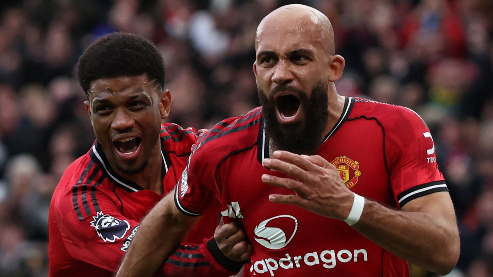 Des joueurs de Manchester United célébrant un but crucial, avec un joueur barbu exultant et un autre en tenue rouge et noire.