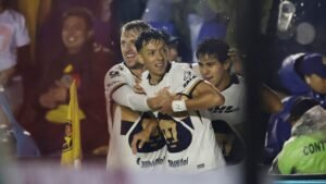 Jorge Ruvalcaba célèbre avec ses coéquipiers après avoir marqué, portant le maillot blanc des Pumas UNAM, avec en arrière-plan un terrain détrempé par la pluie pendant un match.