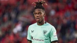 Nico Williams portant un maillot de l'Athletic Bilbao vert menthe, l'air inquiet lors d'un match, devant des sièges de stade rouges.