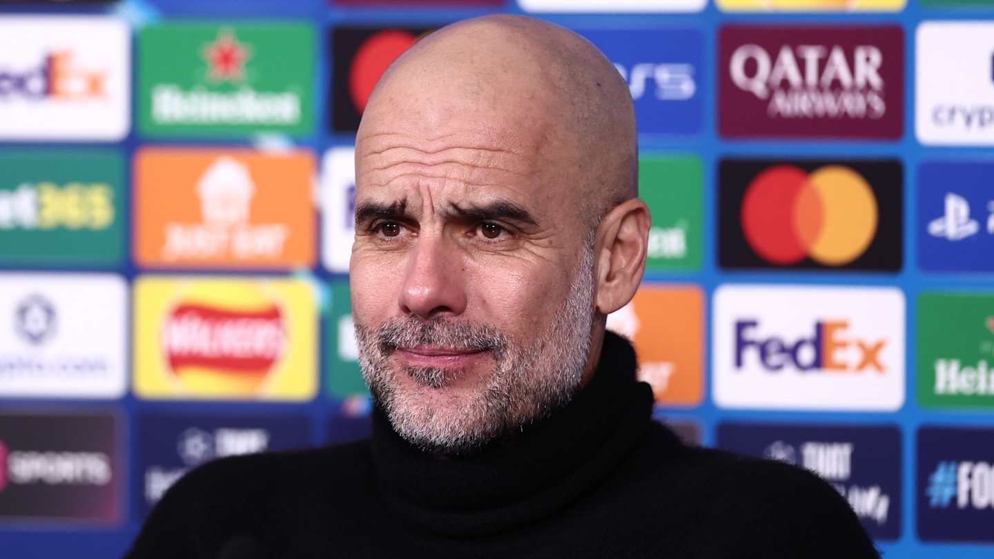 Pep Guardiola at a press conference, wearing a black turtleneck, with a backdrop of sponsor logos including Heineken and Mastercard.