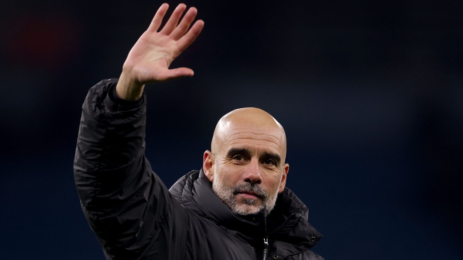 Pep Guardiola salue les supporters, vêtu d'une veste noire, affichant un calme serein malgré les spéculations persistantes sur son avenir à Manchester City.