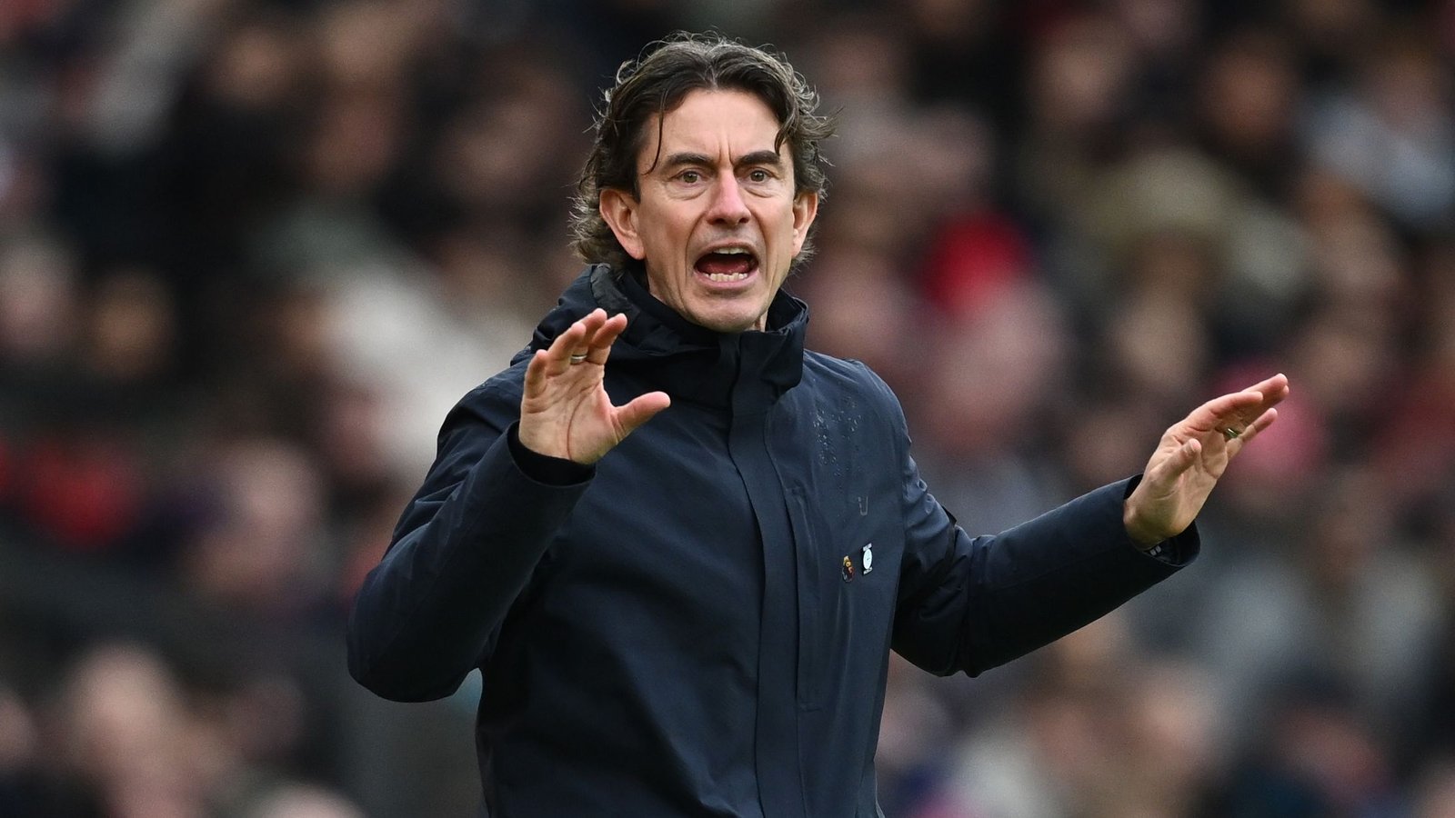 Brentford manager Thomas Frank passionately gestures during a match, wearing a dark coat and displaying intense focus on the game.