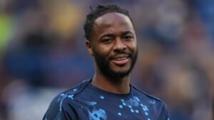 Raheem Sterling glimlacht tijdens de warming-up in een blauw trainingspak met een spattenpatroon, wat zijn toewijding toont vóór een wedstrijd.