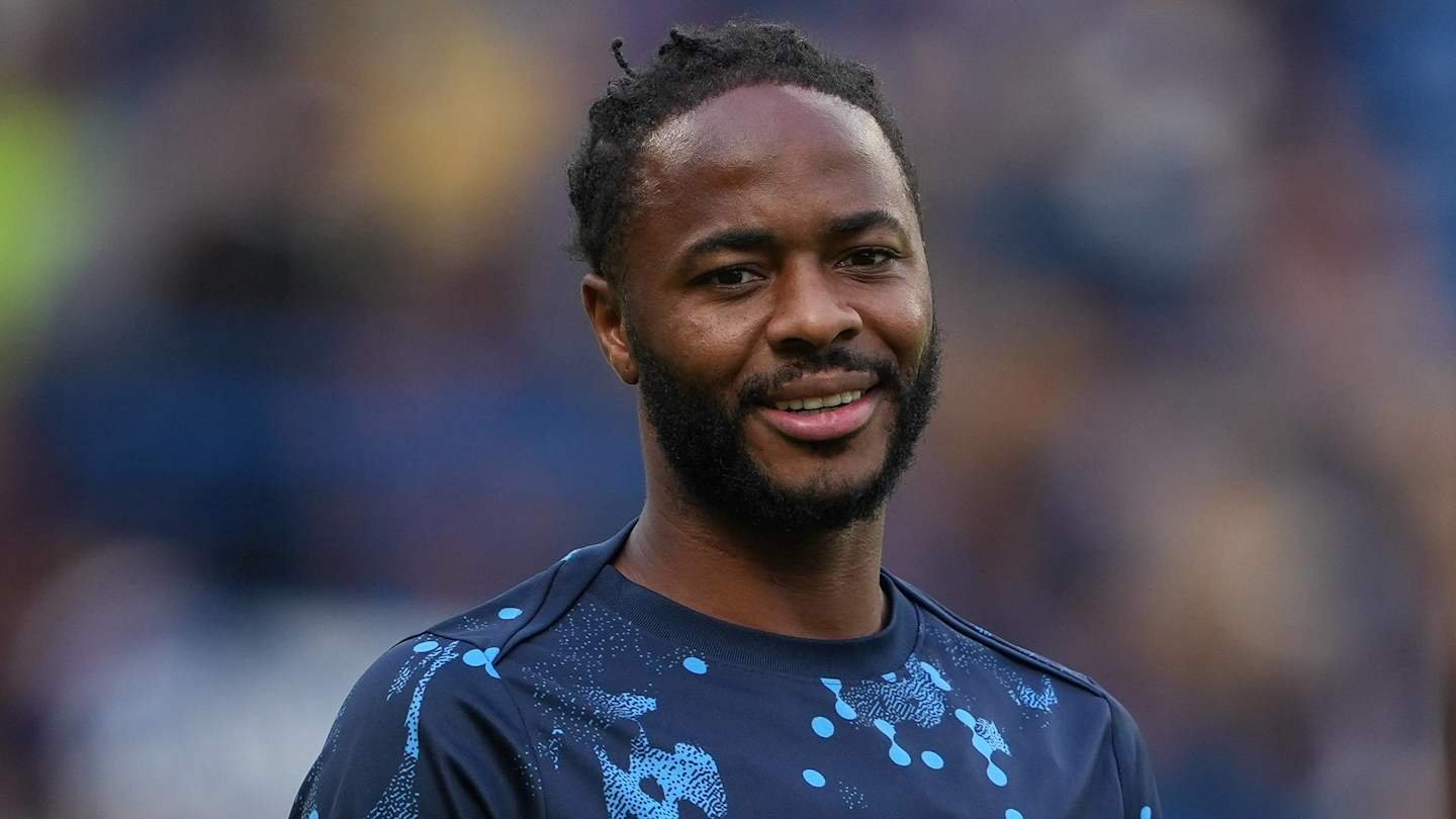 Raheem Sterling glimlacht tijdens de warming-up in een blauw trainingspak met een spattenpatroon, wat zijn toewijding toont vóór een wedstrijd.