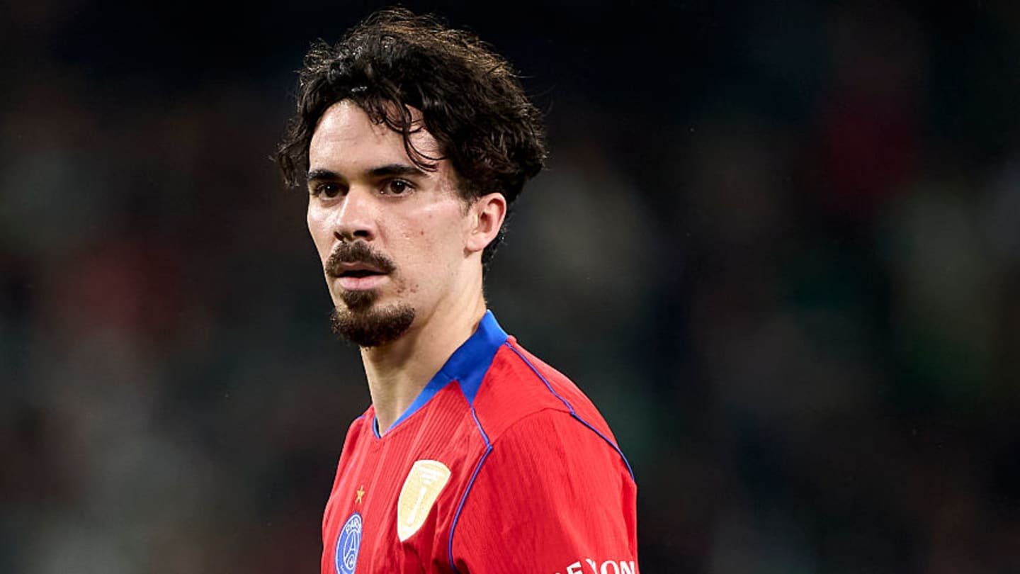 Red-shirted Moroccan footballer stands on the pitch, focused, during a match, showcasing intensity and determination.