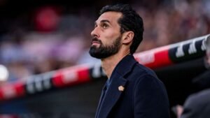 Moroccan football manager reflecting on the match from the sidelines, dressed in a dark coat with a focused expression.