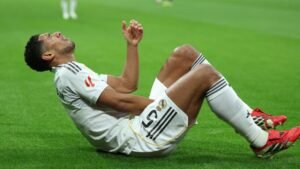 Jude Bellingham op het veld, die na een blessure tijdens een wedstrijd pijn uitdrukt, gekleed in het witte Real Madrid-tenue met rode schoenen.