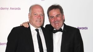 Richard Keys et Andy Gray posent ensemble lors d'un événement, tous deux en costume noir formel avec cravate, souriant devant un fond blanc.