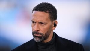 Rio Ferdinand, l'air sérieux et portant un manteau noir, pendant une discussion, mettant en lumière ses expériences dans le football.
