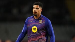 Ronald Araujo en haut d'entraînement vibrant du FC Barcelone, concentré et marchant sur le terrain, reflétant la détermination et la préparation.