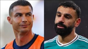 Cristiano Ronaldo and Mohamed Salah in close-up, both looking towards the viewer; Ronaldo in an orange training top, Salah in a green kit.