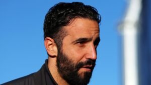 Portrait de Ruben Amorim, portant une veste sombre, avec un ciel bleu en arrière-plan, réfléchissant à son récent licenciement de Manchester United.